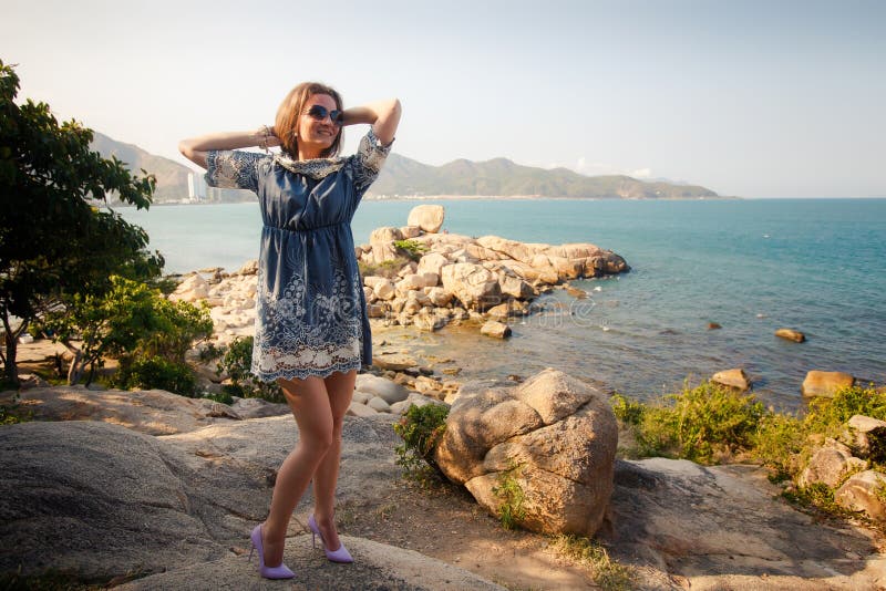 girl in short grey frock stands on rocks by sea against city