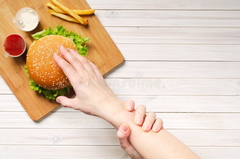 The girl shows willpower by holding with her left hand, her right hand that reaches for a hamburger. Diet and healthy nutrition