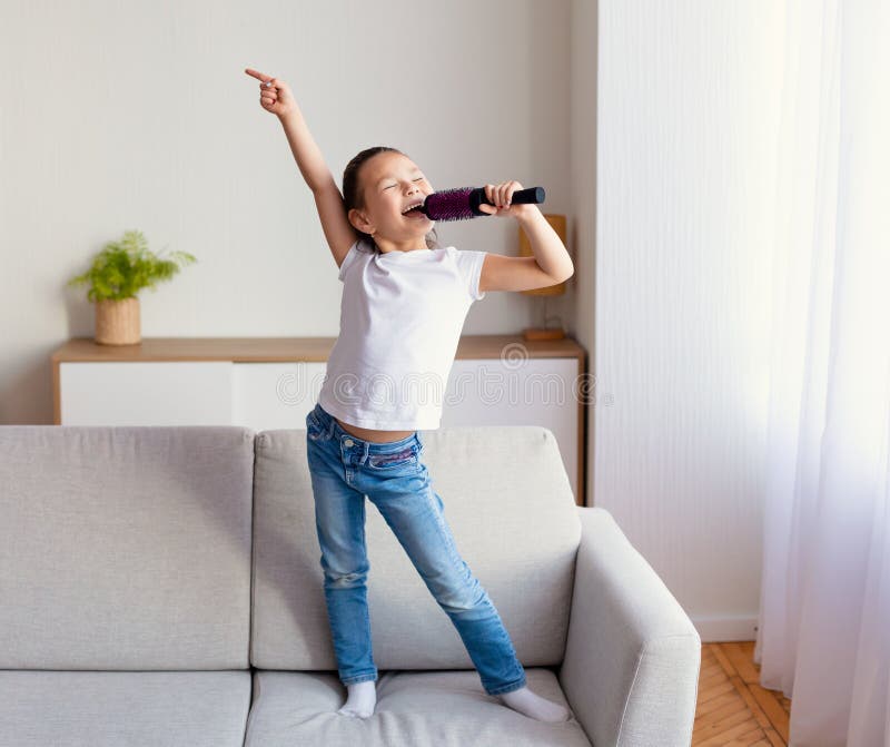 Girl Singing Holding Hairbrush Like Microphone Standing On Sofa Indo