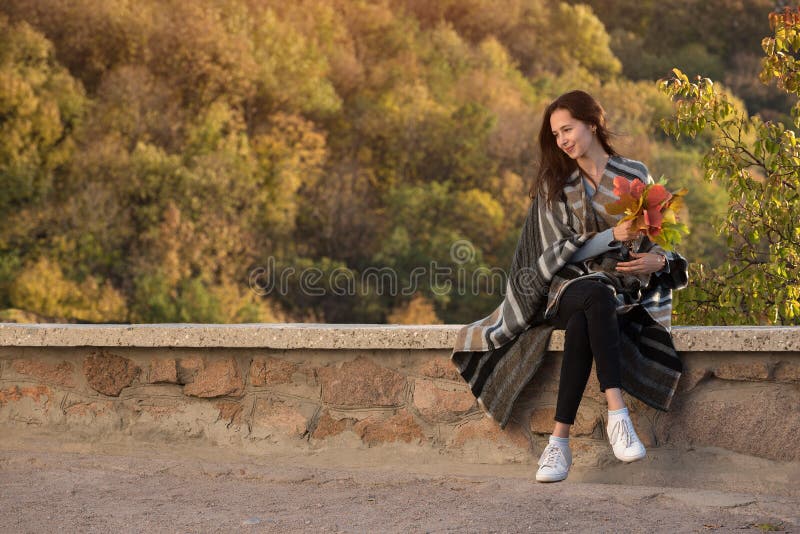 Girl sits on background of nature with a bouquet of fall leaves. Travel in the autumn