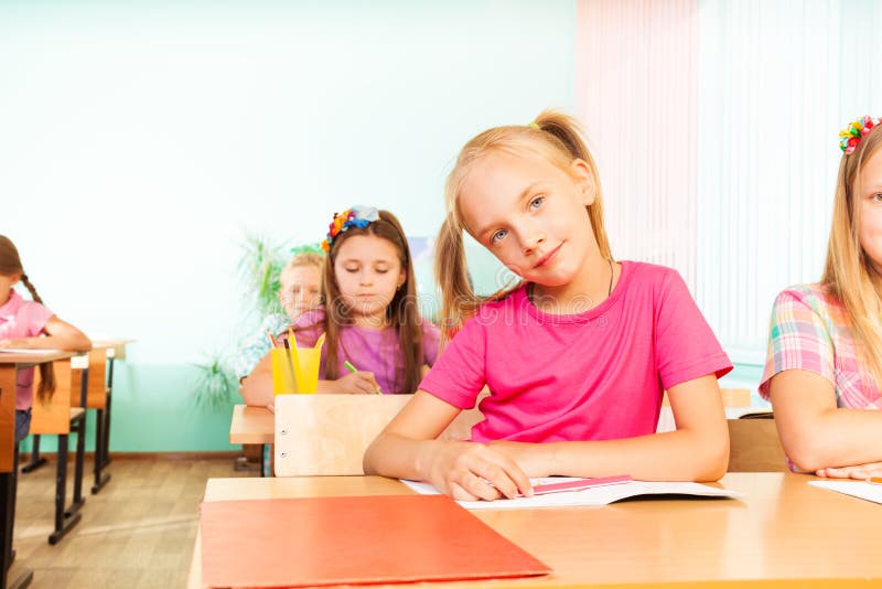 Girl sits at desk with elbows on exercise book royalty free stock photography