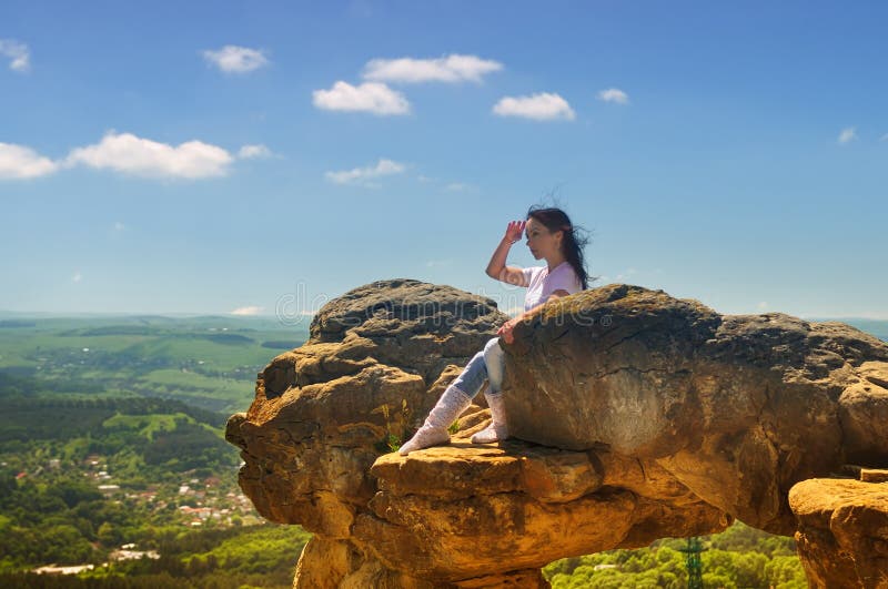 A girl sits on the edge of a cliff and looking into the distance