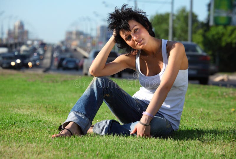 Girl sits on lawn at road in city