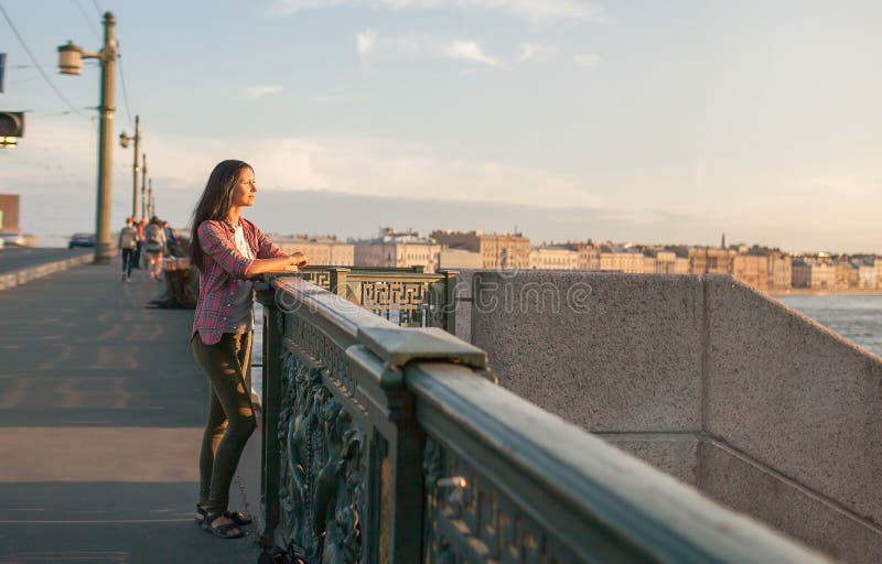 An informal-looking girl . sitting on the bridge in the morning in the city, meditating, relaxing and dreaming. the concept of travel, personal harmony and personal growth, peace of mind