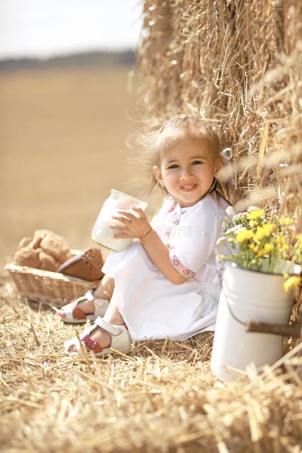 Girl is sitting in a field by a haystack with a can of fresh steamed cow`s milk.