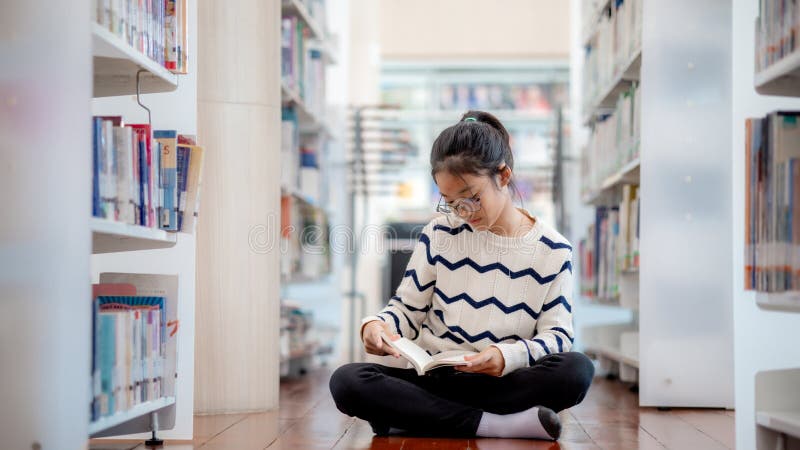 A girl is sitting on the floor in a library reading a book stock photography