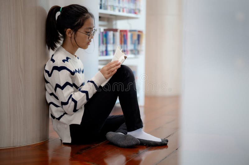 A girl is sitting on the floor reading a book stock image