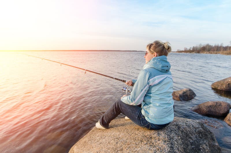 Girl sitting on a rock with a fishing rod.