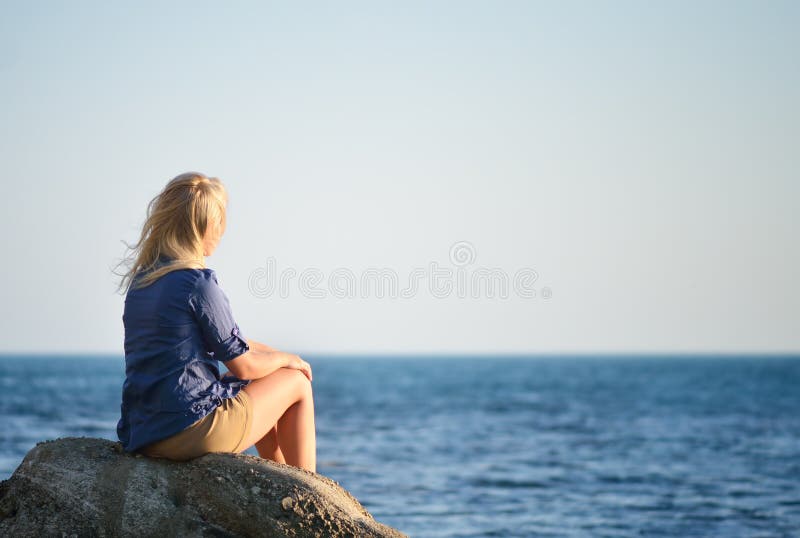 Girl is sitting on a rock and looking at the sea