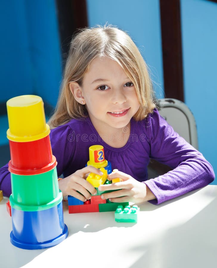 Portrait of cute girl sitting with toys at desk in preschool