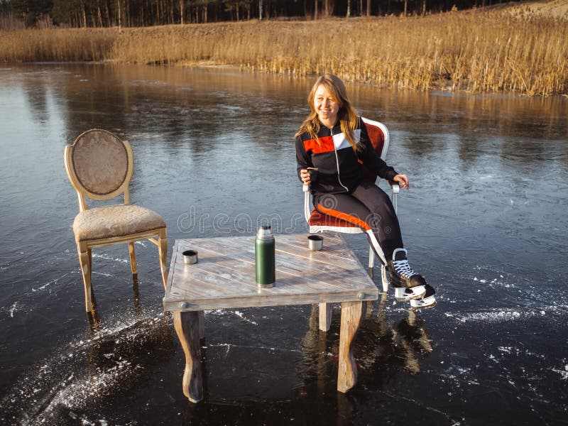 A girl in skates sits at a table on a frozen lake in the forest. Thermos Tea Party