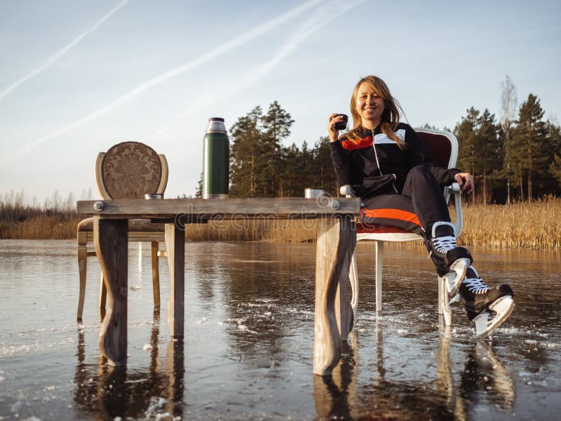 A girl in skates sits at a table on a frozen lake in the forest. Thermos Tea Party