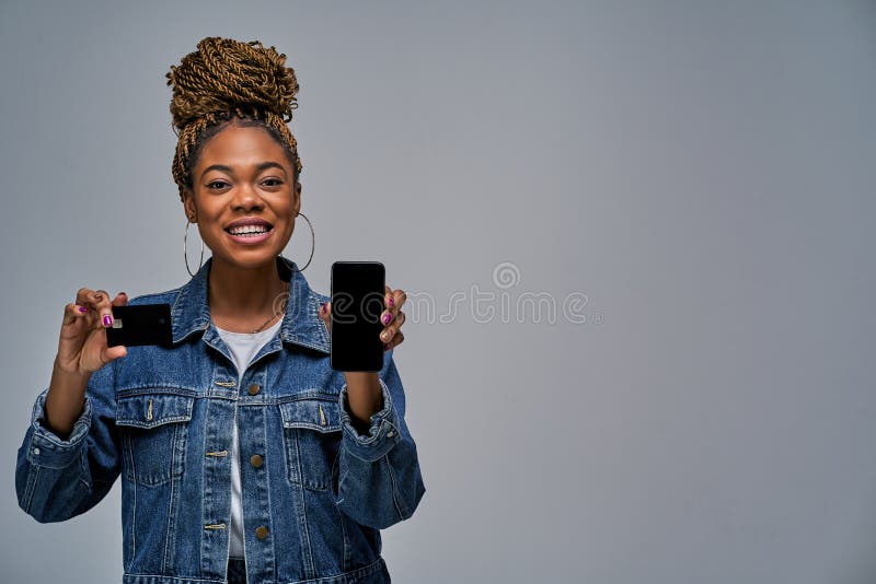 A Girl with a Smile with Hair Style in a Jeans Jacket Holds Smartphone in  One Hand and Shows a Black Card in the Other Hand. Stock Image - Image of  confident,