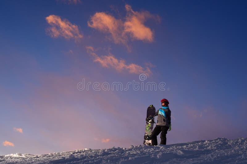 Girl snowboarder stands on a hillside against dark sunset sky. Girl snowboarder stands on a hillside against the dark sunset sky royalty free stock image Girl snowboarder stands on a hillside against dark sunset sky. Girl snowboarder stands on a hillside against the dark sunset sky royalty free stock image
