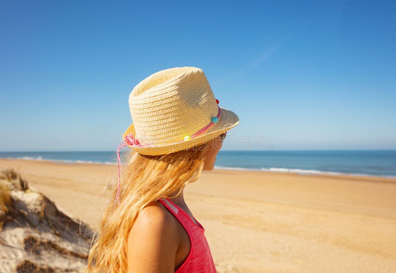 Girl in straw hat looks at sea view from behind