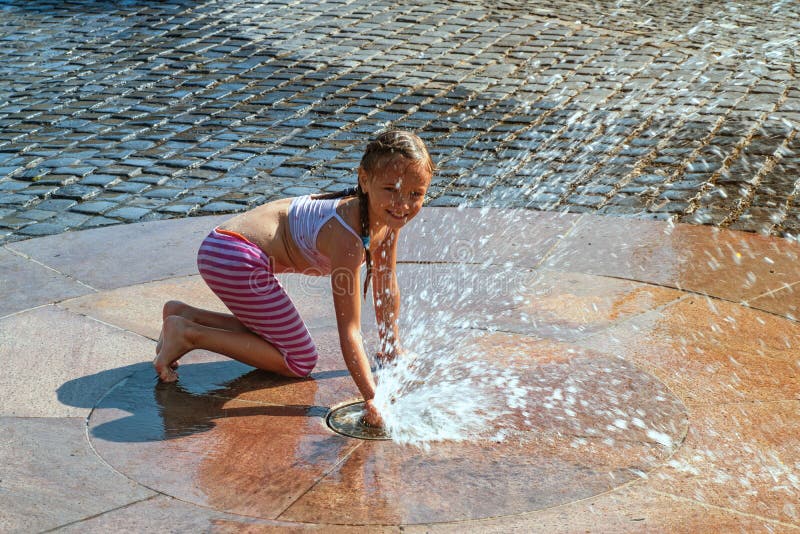 Girl happily in shallow clean water on of city fountain on warm. 