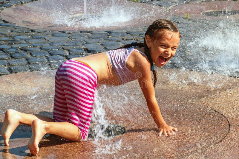 Girl on a sunny warm day playing outside in a water fountain. Girl happily in shallow clean water on of city fountain on warm