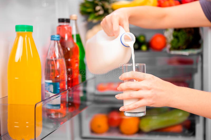 The girl takes a bottle of milk from the refrigerator and pours it into a clear glass, small depth of field bright lighting