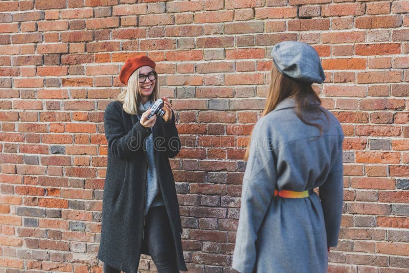 Girl takes picture of her female friend in front of brick wall in urban street - photographer and youth urban lifestyle royalty free stock images