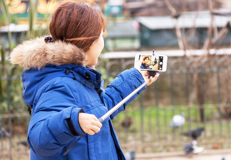 Girl is taking selfie (photo) with smartphone and monopod (stick)