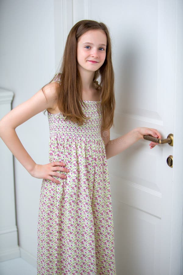 Girl teenager in a smart dress standing near the white door.