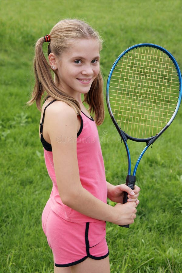 Happy teenage girl in sport outfit with tennis racket on green grass background. Happy teenage girl in sport outfit with tennis racket on green grass background