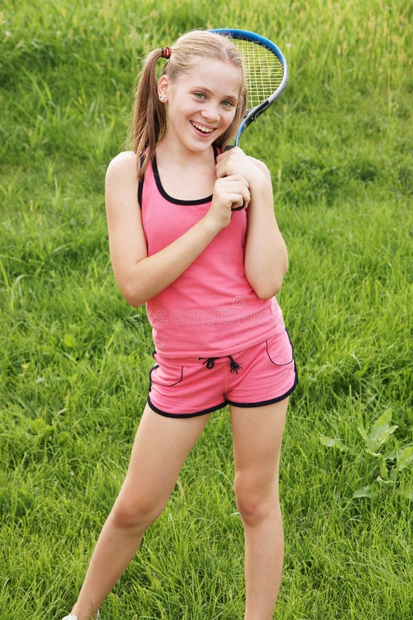 Happy teenage girl in sport outfits with tennis racket on green grass background. Happy teenage girl in sport outfits with tennis racket on green grass background