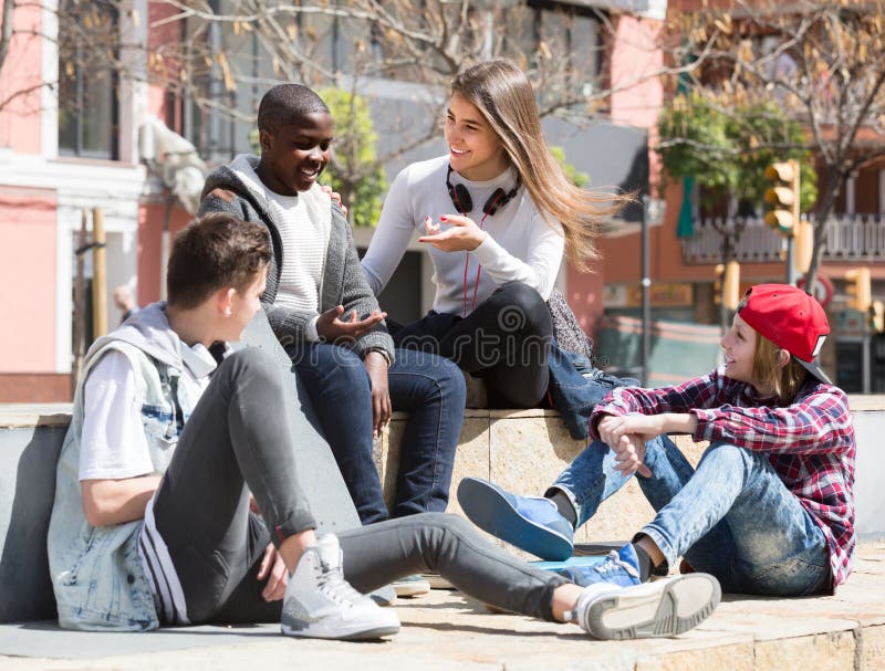 Girl and three boys hanging out outdoors and discussing something