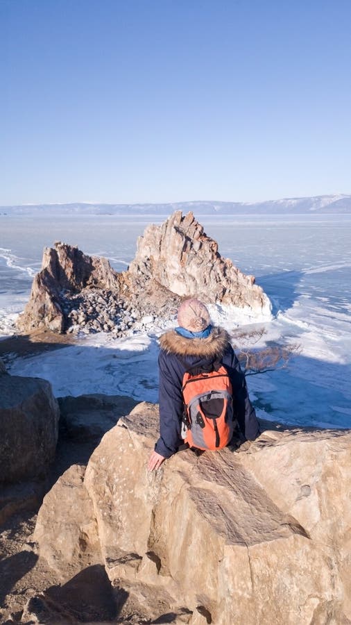 Girl traveler in warm clothes in winter sitting on Cape Burhan and admires the rock Shaman on the island of Olkhon on lake Baikal. stock photos Girl traveler in warm clothes in winter sitting on Cape Burhan and admires the rock Shaman on the island of Olkhon on lake Baikal. stock photos