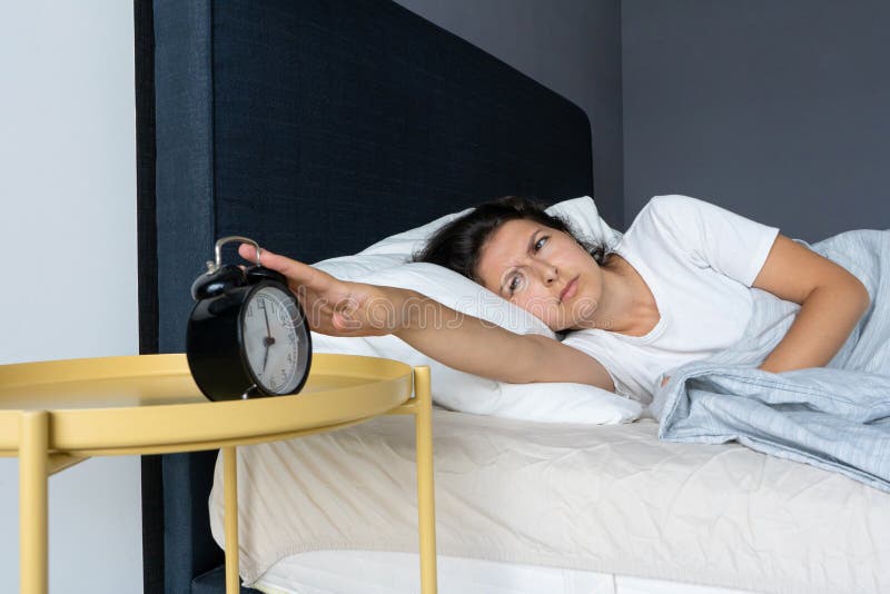The girl turns off the annoying alarm clock to continue sleeping. Get some more sleep. It is a hard morning. Time to wake up royalty free stock photos The girl turns off the annoying alarm clock to continue sleeping. Get some more sleep. It is a hard morning. Time to wake up royalty free stock photos