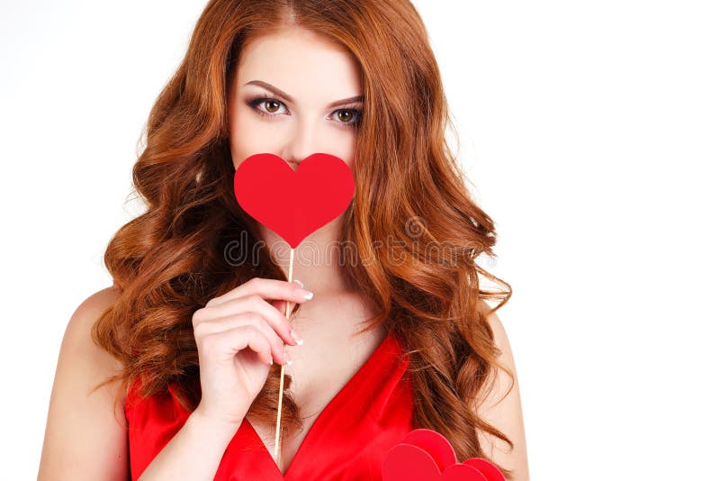 Beautiful young woman with long brown hair, bright makeup, brown eyes, and a red dress with a little red hearts on a stick, a symbol of love, on a white background. Beautiful young woman with long brown hair, bright makeup, brown eyes, and a red dress with a little red hearts on a stick, a symbol of love, on a white background.