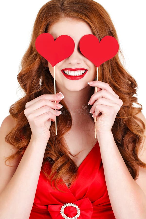 Beautiful young woman with long brown hair, bright makeup, brown eyes, and a red dress with a little red hearts on a stick, a symbol of love, on a white background. Beautiful young woman with long brown hair, bright makeup, brown eyes, and a red dress with a little red hearts on a stick, a symbol of love, on a white background.