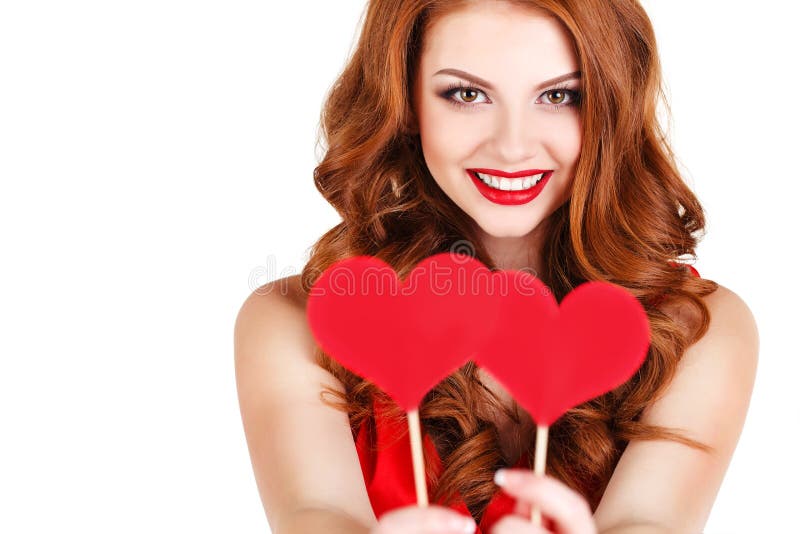 Beautiful young woman with long brown hair, bright makeup, brown eyes, and a red dress with a little red hearts on a stick, a symbol of love, on a white background. Beautiful young woman with long brown hair, bright makeup, brown eyes, and a red dress with a little red hearts on a stick, a symbol of love, on a white background.