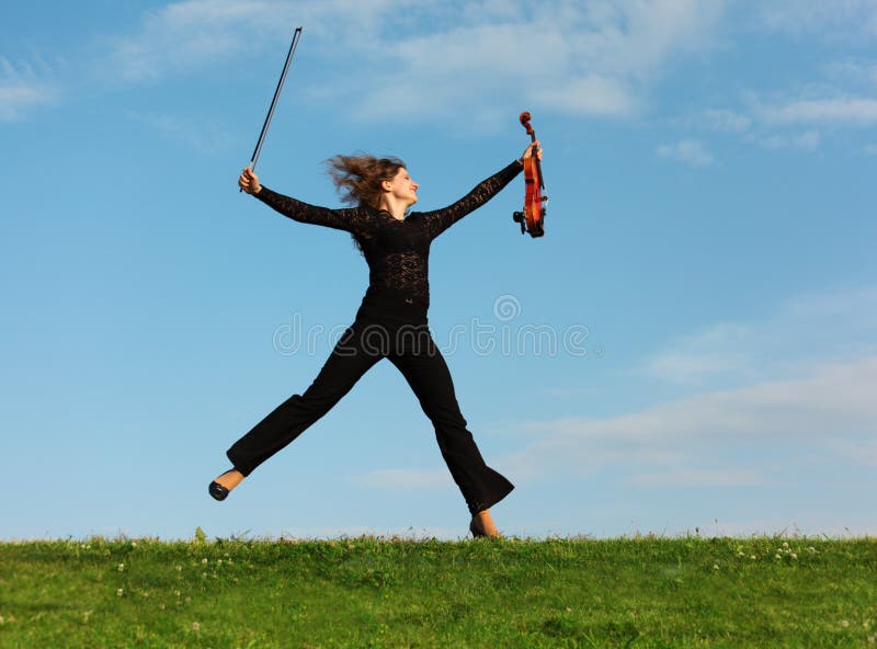 Girl with violin jumps against sky