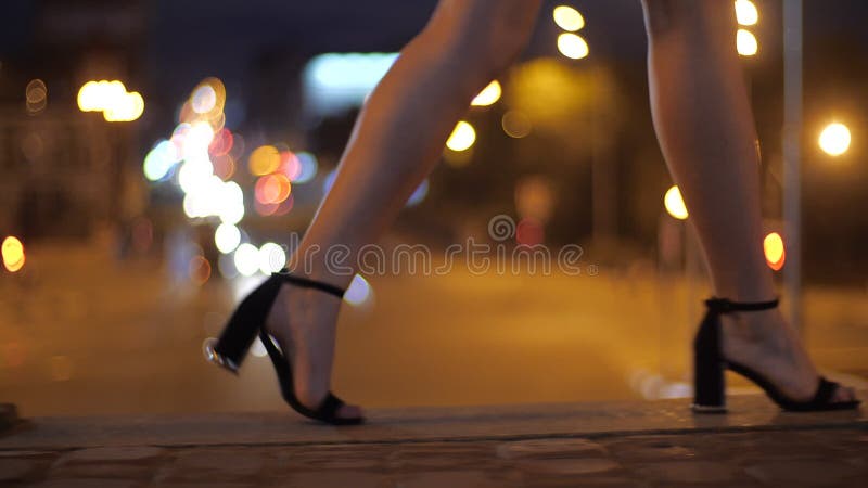 Girl walks on a city bridge over the highway in beautiful heels, legs with heels close-up. Walk in the evening city in