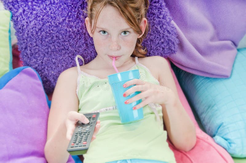 Young girl with drink watching TV in bed royalty free stock photo. 