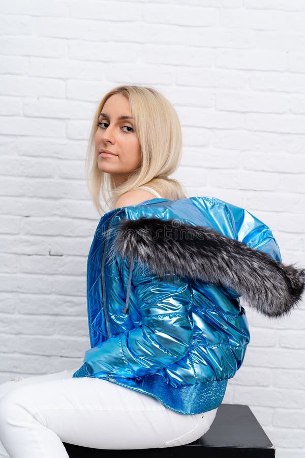 The girl is wearing white jeans, a white blouse, and a blue jacket with a fur hood on a white background. stock photography
