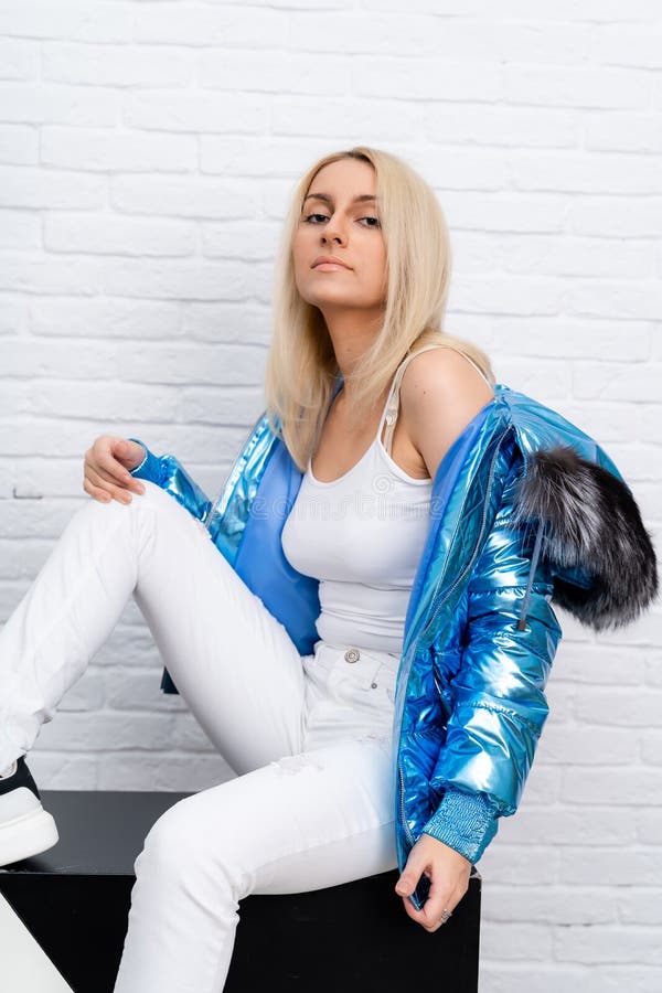 The girl is wearing white jeans, a white blouse, and a blue jacket with a fur hood on a white background. royalty free stock photo