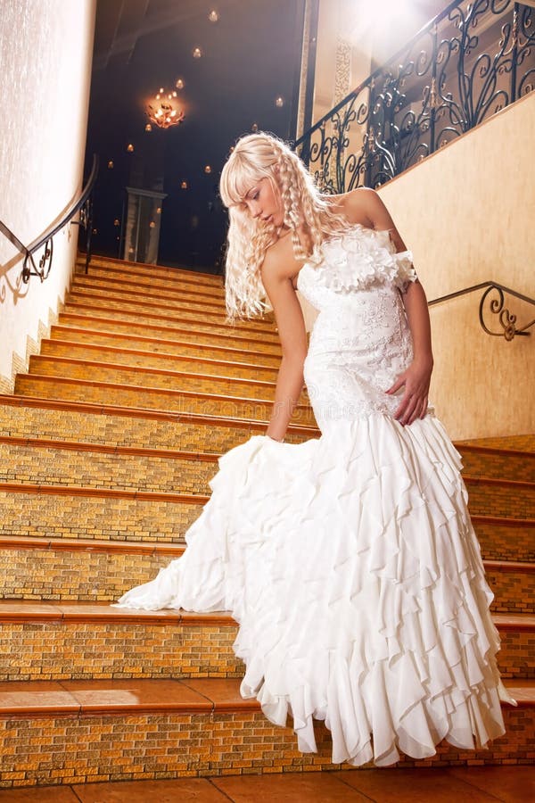 Krásna blondínka v svadobné šaty ísť dole po schodoch.
