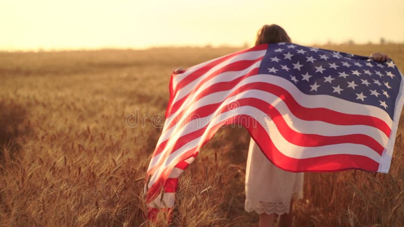 Girl in white dress wearing an American flag while running in a beautiful wheat field