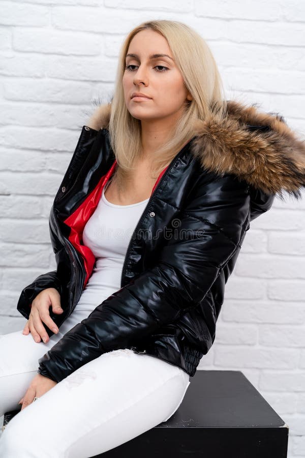 A girl in white jeans, a white blouse and a black shiny jacket with a fur hood on a white background. royalty free stock photos