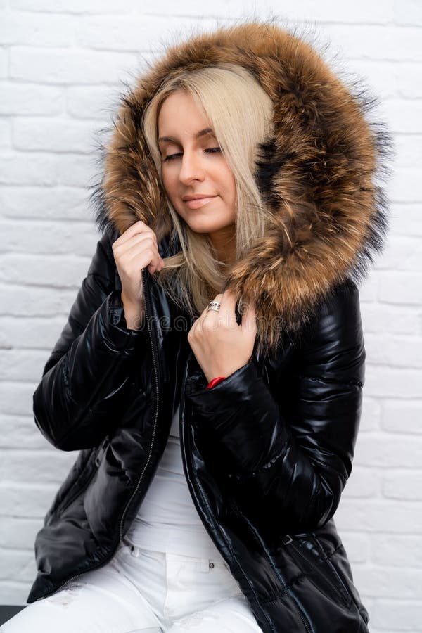 A girl in white jeans, a white blouse and a black shiny jacket with a fur hood on a white background. stock photos
