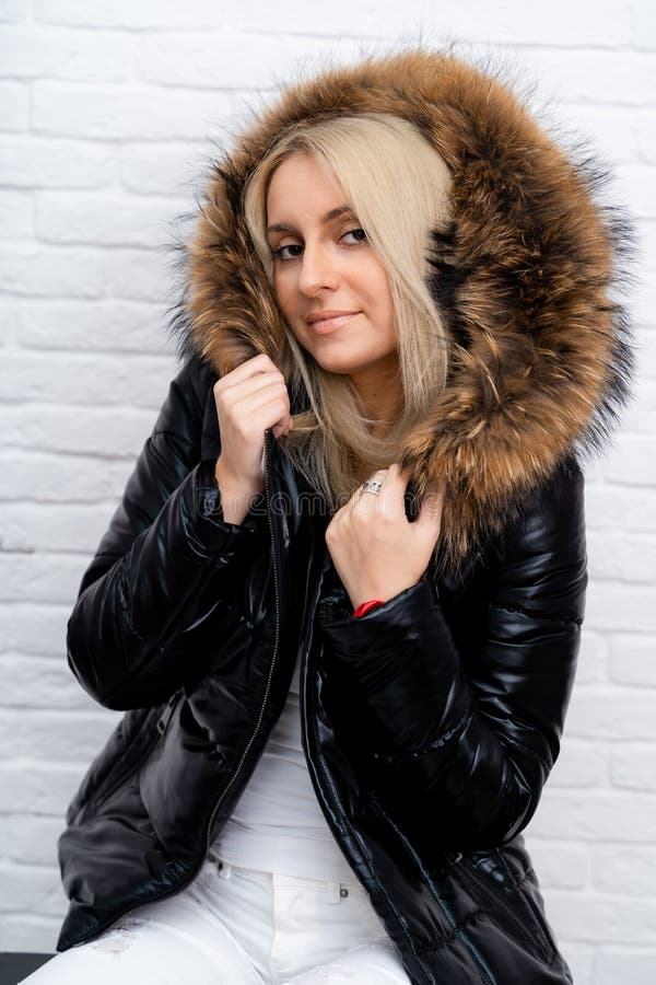 A girl in white jeans, a white blouse and a black shiny jacket with a fur hood on a white background. stock images