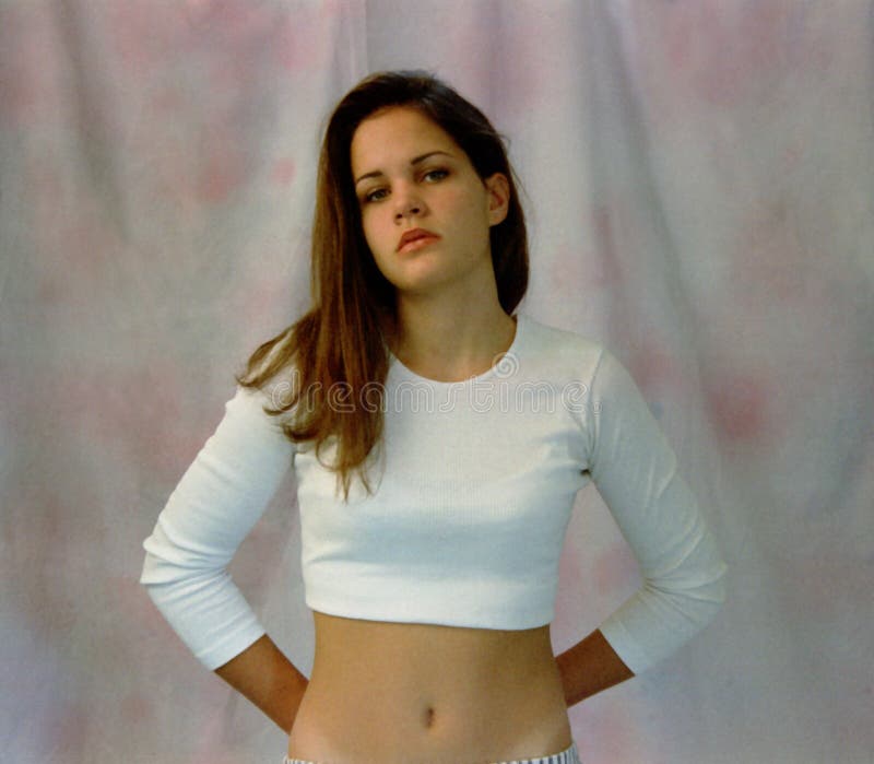Teen girl with long brunette hair in long sleeved white, belly-button barin...