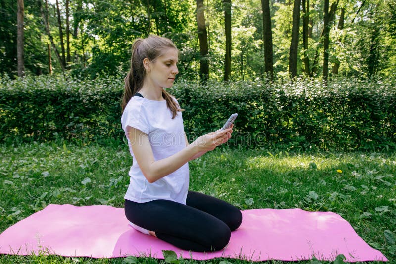 A Girl in a White T-shirt and Black Leggings on a Pink Mat on a Summer  Green Lawn and Talking by Video Call on the Phone Stock Image - Image of  legs,