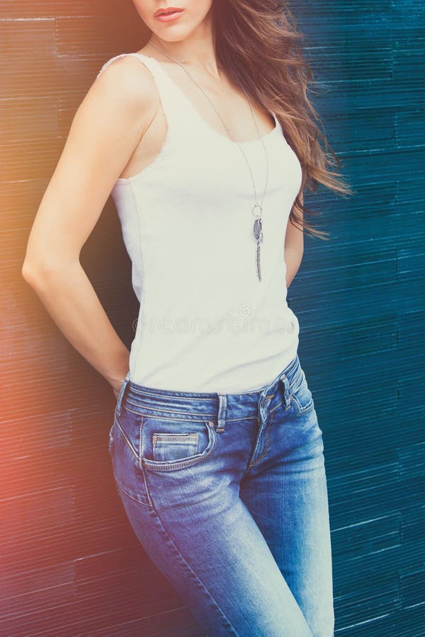 Girl in white tank shirt and blue jeans outdoor summer day lean on tiled wall