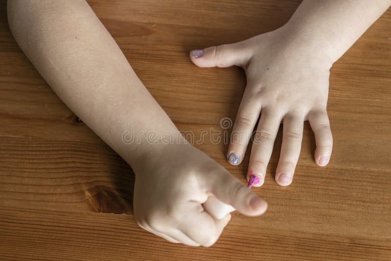 Hands of a little girl who paints her nails with nail polish behind a wooden stall