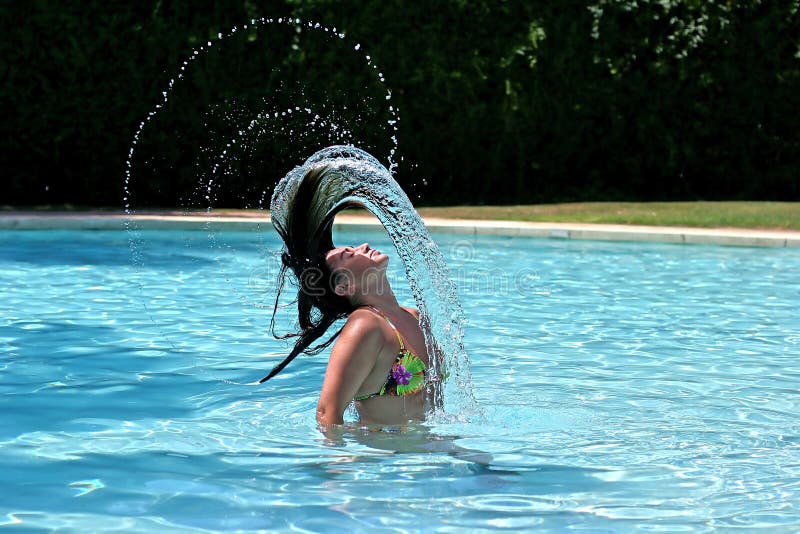 Girl or woman in blue sunny swimming pool throwing wet hair back spraying water everywhere. Girl or woman in blue sunny swimming pool throwing wet hair back spraying water everywhere.