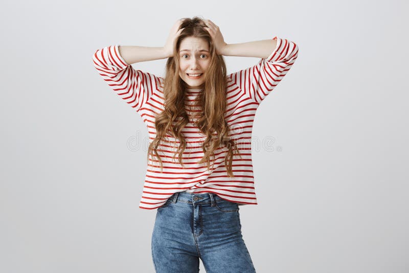 Girl is worried and puzzled, having lots of work and no time. Portrait of bothered anxious woman holding hands on hair, smiling awkwardly, remembering important information she forgot, being in rush.