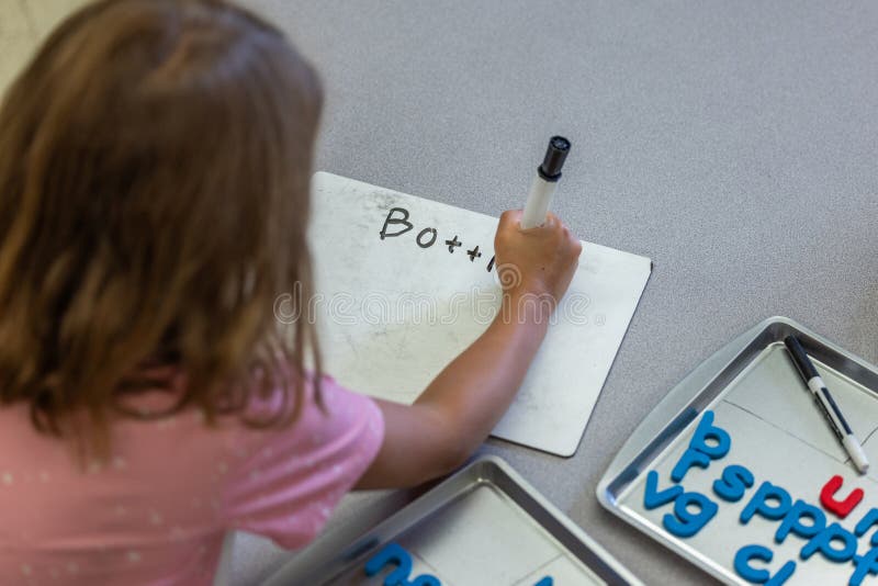 A girl is writing on a white board leaning spelling stock photo